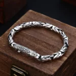 Om Mani Padme Hum Dorje Vajra copper bracelet overhead flat lay view on wooden storage box, showing detailed braided chain and engraved clasp