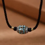 Tibetan Om Mani Padme Hum Dzi bead necklace with braided black rope chain and turquoise-inlaid pendant on brown fabric background