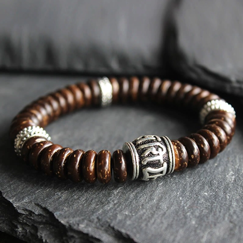 Close-up detail of engraved Sanskrit Om Mani Padme Hum mantra bead with silver spacer rings on brown coconut shell bracelet
