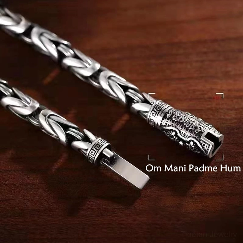 Om Mani Padme Hum engraved clasp detail of Tibetan copper bracelet showing mantra text and braided silver chain on dark wood