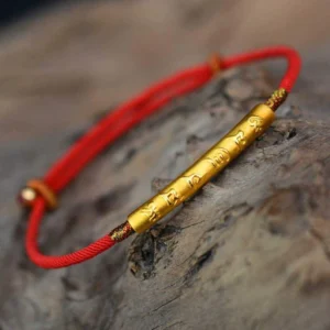 Om Mani Padme Hum mantra bracelet with gold-engraved sterling silver charm tube and braided red cord on wooden surface
