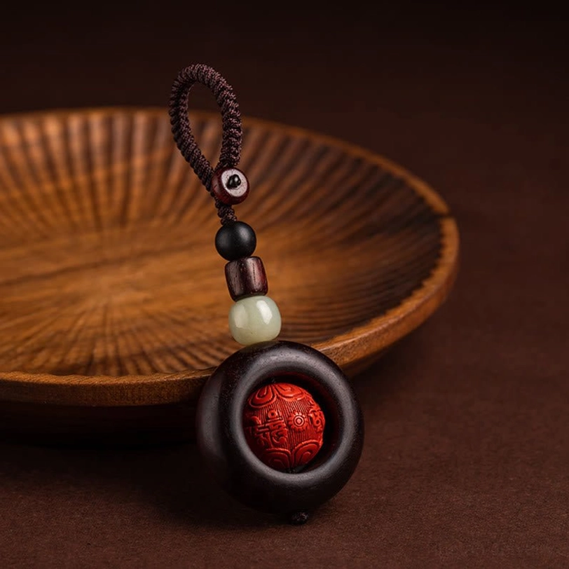 Single Tibetan Om Mani Padme Hum protection keychain with carved cinnabar bead and braided cord three-quarter view