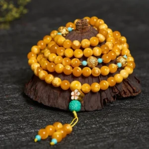 Close-up overhead view of amber prayer beads showing individual bead details, gold metal spacers, and turquoise tassel pendant on display stand