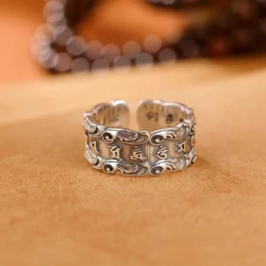Om Mani Padme Hum Buddhist mantra ring front view, aged silver tone with embossed mantras and lotus patterns, displayed with prayer beads