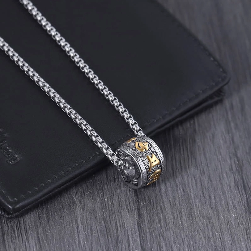 Single Om Mani Padme Hum two-tone rotating necklace pendant with wheat chain on wooden table flat lay beside leather wallet