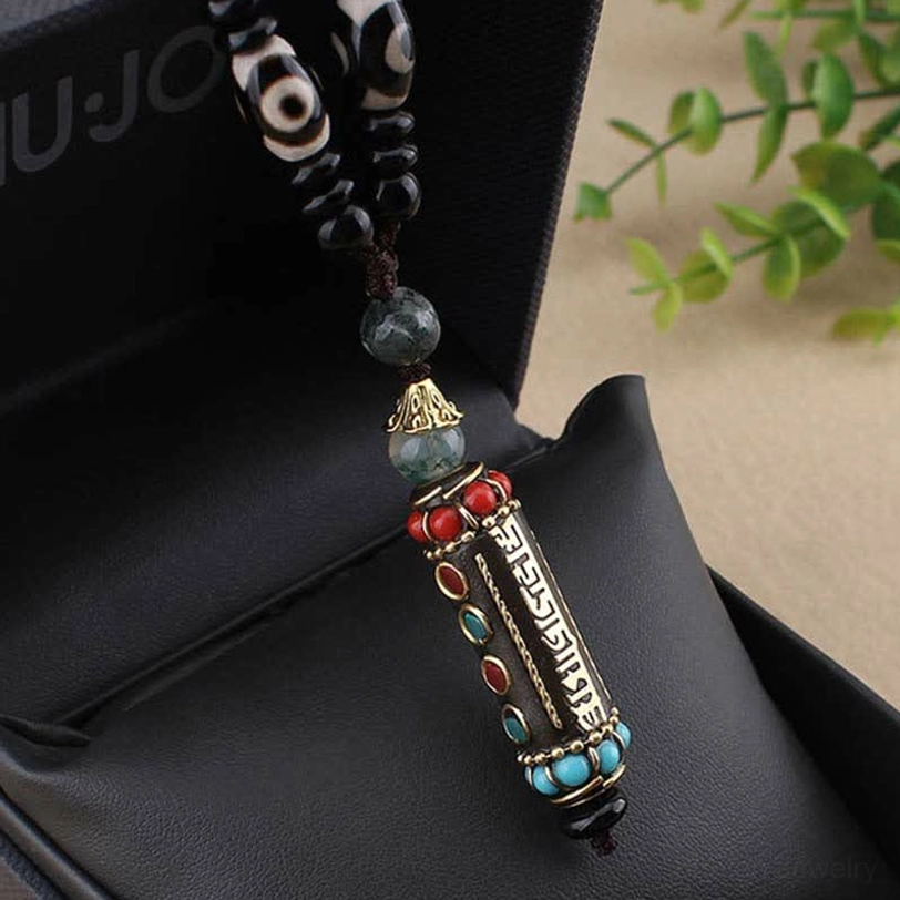 Close-up detail of Om Mani Padme Hum enamel pendant with Sanskrit mantra and dzi bead accents