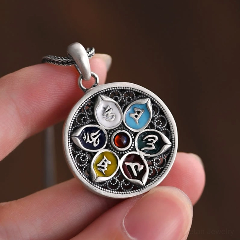 Tibetan pendant held between fingertips showing hollow filigree details and sacred mantra carving