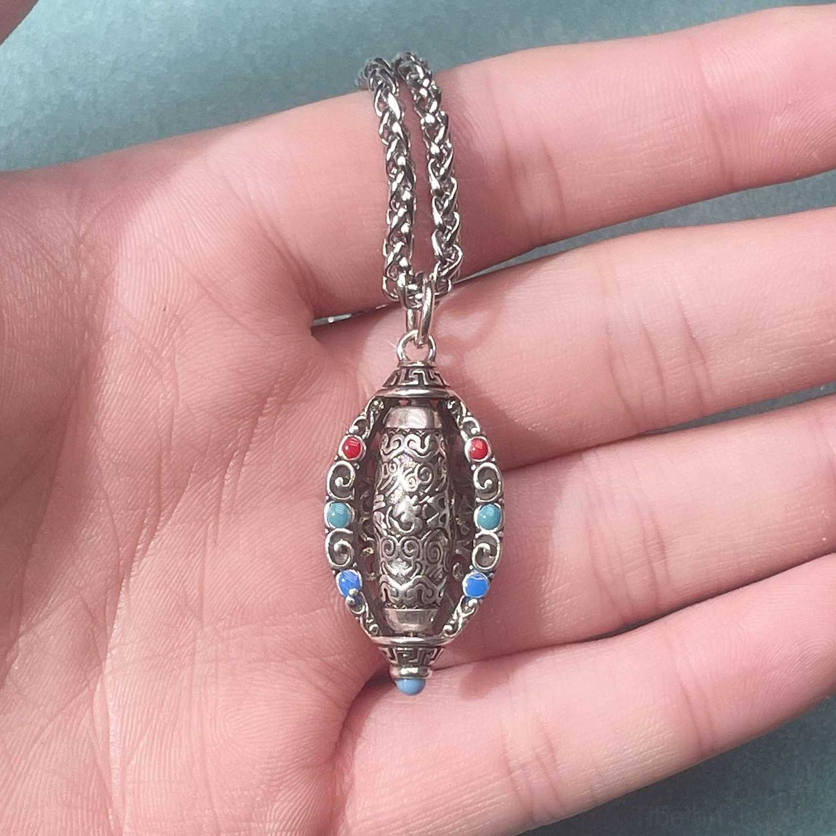 Rotatable Tibetan Om Mani Padme Hum pendant held in palm showing clear view of gemstone arrangement carved patterns and vintage silver metal