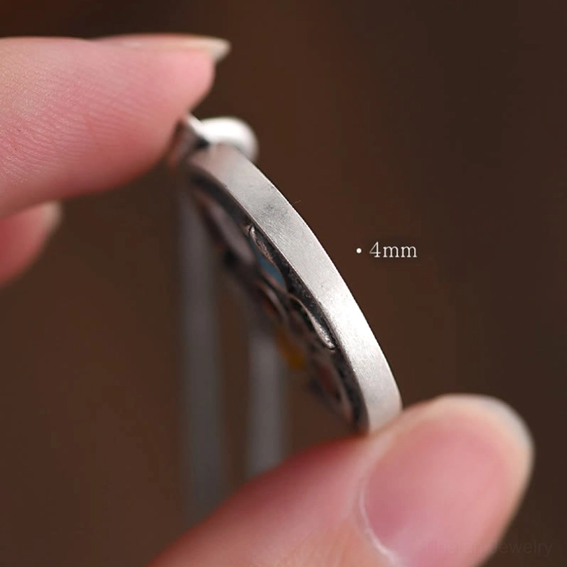 Tibetan pendant side view held in finger showing 4mm thickness, smooth silver edge, and hollow pendant structure