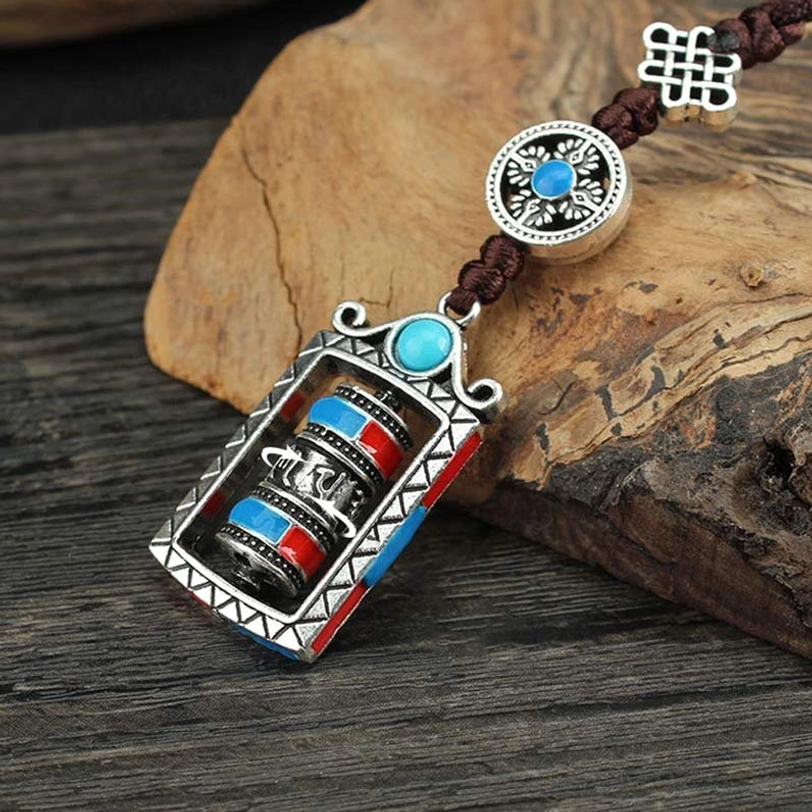 Tibetan prayer wheel pendant oblique side view, turquoise blue with rotatable mechanism, triangular frame trim, dark brown rope on wooden surface