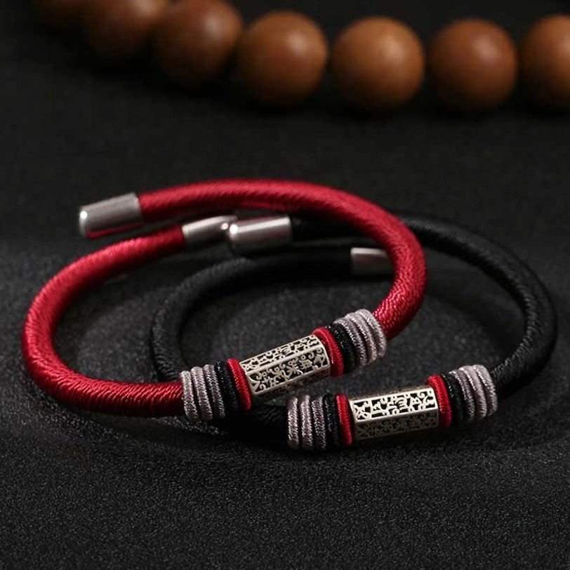 Single Om Mani Padme Hum red string bracelet with silver engraved charm and thread wraps on leather backdrop