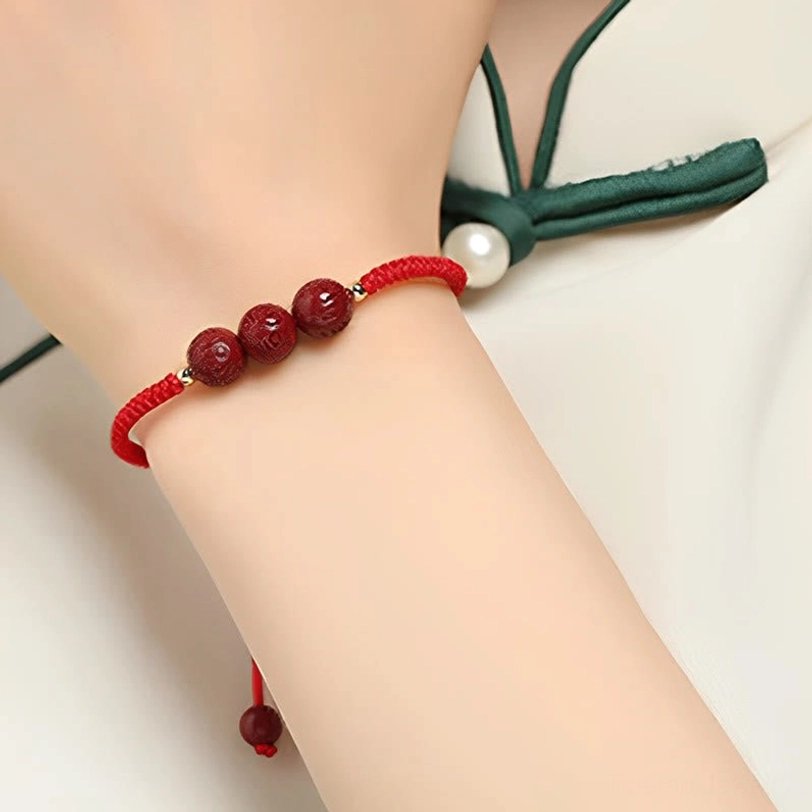 Cinnabar Om Mani Padme Hum bracelet worn on wrist featuring red woven cord and carved red beads, side close-up view