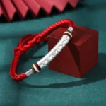 Om Mani Padme Hum sterling silver red string protection bracelet with engraved mantra tube on vintage dark table