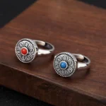Tibetan Om Mani Padme Hum adjustable copper rings in red and blue gemstone styles, vintage silver finish, displayed on dark wooden surface with mantra engravings visible