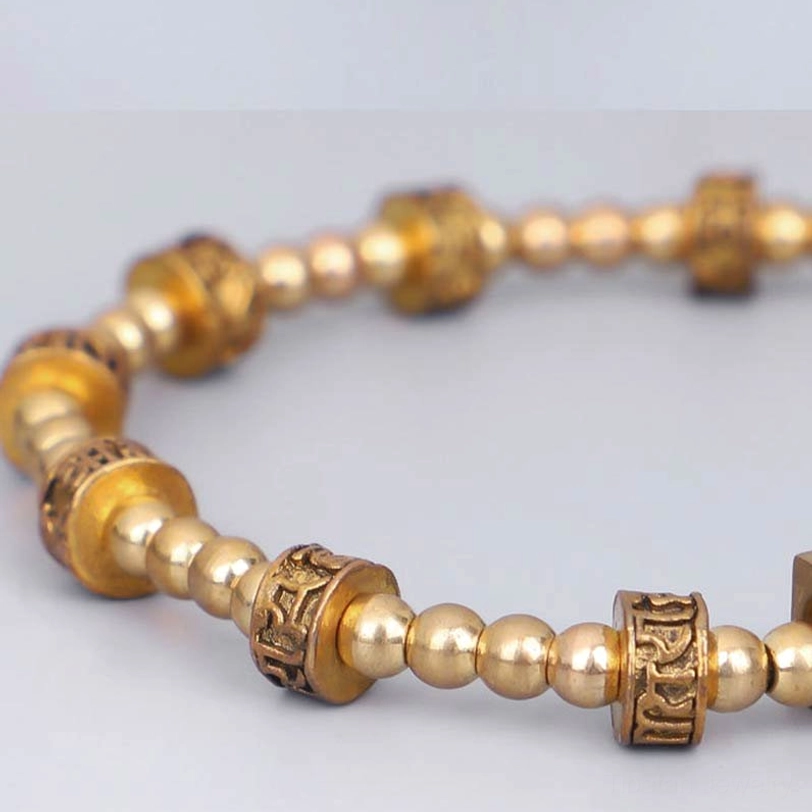 Close-up macro shot of embossed Om Mani Padme Hum characters on brass cylindrical beads