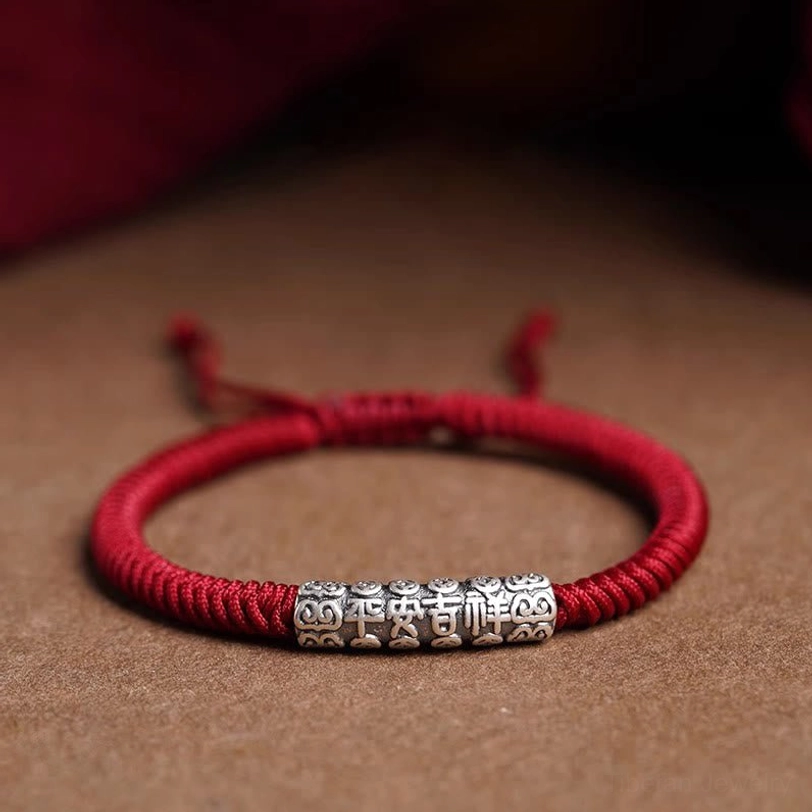 Handmade Tibetan Om Mani Padme Hum sterling silver rope bracelet with dark red cord, top-down flat lay view showing adjustable knot