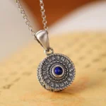 925 Sterling Silver Om Mani Padme Hum pendant with lapis lazuli stone displayed on ancient Buddhist scriptures, showing front overhead view with engraved mantras and twisted decorative border