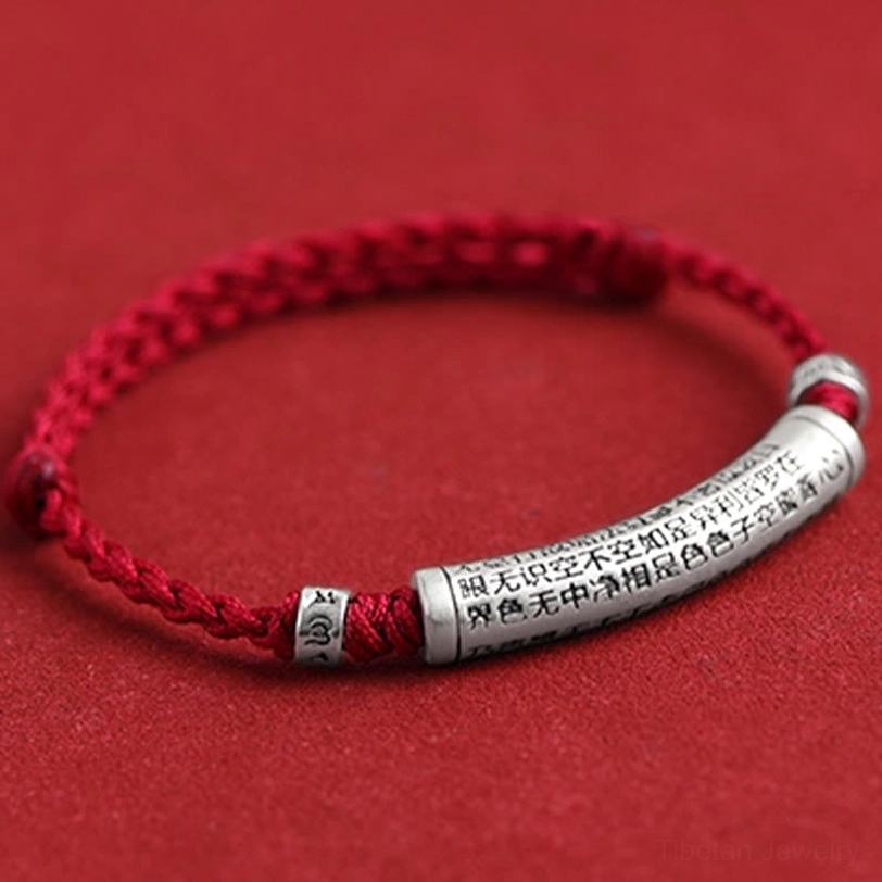 Close-up detail of tibetan protection bracelet showing laser-engraved Heart Sutra on 999 sterling silver tube with braided red rope