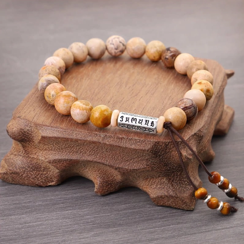 Tibetan mantra prayer bracelet on wooden display stand, flat lay showing adjustable string and silver charm detail