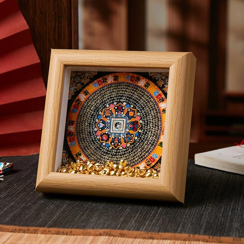 Buddhist thangka frame featuring black-based circular mandala with vibrant colors and golden ingot details on light wood