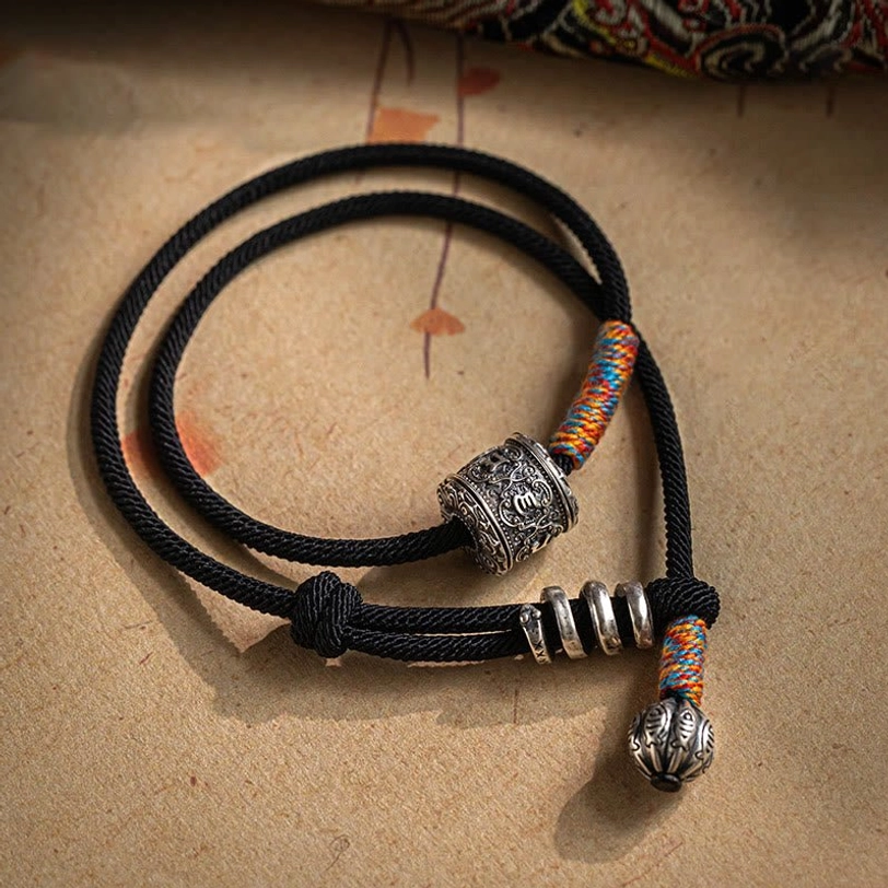 Om Mani Padme Hum Tibetan amulet double wrap bracelet flat lay with carved barrel bead and bell pendant on kraft paper background