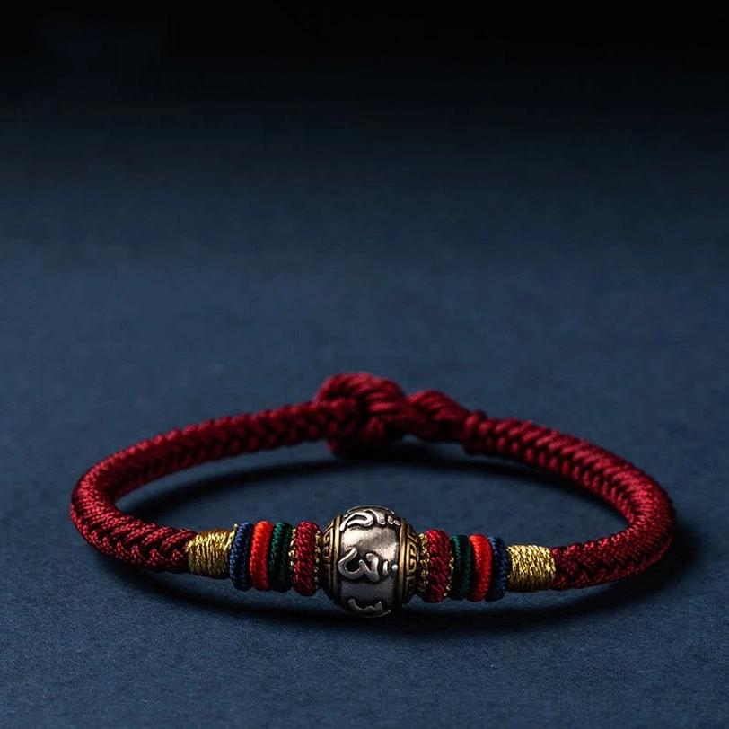 Close-up of red and multicolored Tibetan Om Mani Padme Hum bracelet with 925 sterling silver charm on dark blue background
