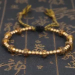 Om Mani Padme Hum gold tibetan mantra bracelet top view with embossed script beads on vintage calligraphy background
