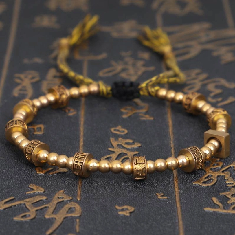 Om Mani Padme Hum gold tibetan mantra bracelet top view with embossed script beads on vintage calligraphy background