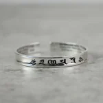 Om Mani Padme Hum white copper cuff bracelet with black engraved Tibetan mantras, flat lay view on grey background