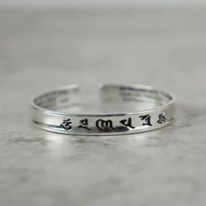 Om Mani Padme Hum white copper cuff bracelet with black engraved Tibetan mantras, flat lay view on grey background