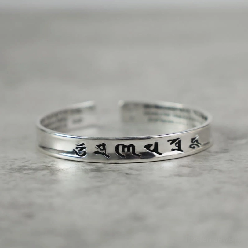 Om Mani Padme Hum white copper cuff bracelet with black engraved Tibetan mantras, flat lay view on grey background