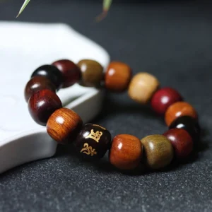 Mixed wood prayer bracelet with golden Sanskrit mantra bead on dark stone surface, flat lay view