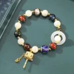 Tibetan prayer wheel charm bracelet with sun stone, tridacna shell, and incense ash liuli glass beads in flat lay on dark green tray