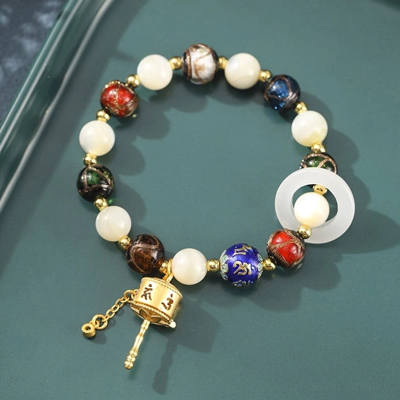 Tibetan prayer wheel charm bracelet with sun stone, tridacna shell, and incense ash liuli glass beads in flat lay on dark green tray
