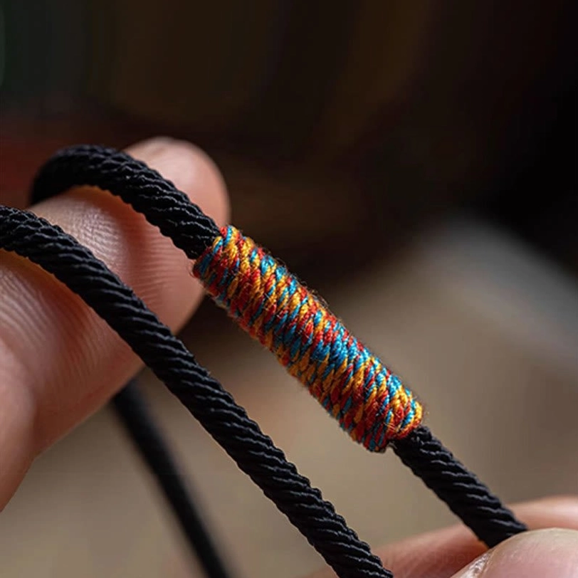 Closeup of Tibetan mantra bracelet cord showing rainbow woven thread detail and black braided material