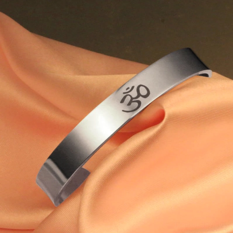 Side view of OM engraved open cuff bangle showing adjustable metal band with etched Om symbol on peach background