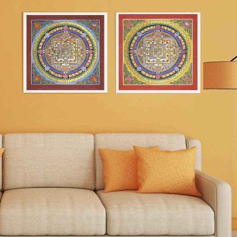 Two framed Kalachakra mandala thangkas with red decorative mats in warm-toned home interior with neutral sofa