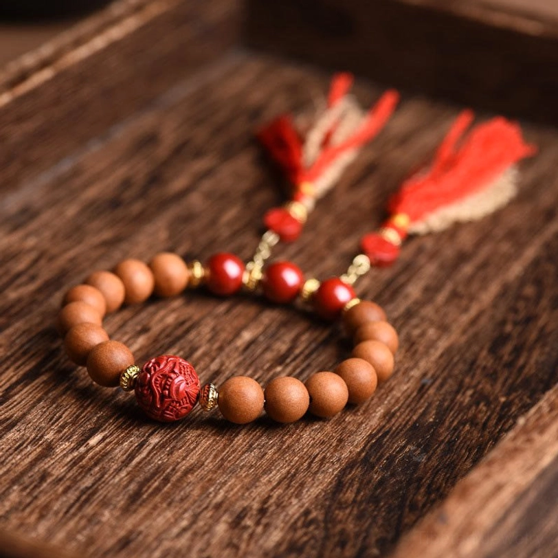 Peach wood cinnabar wealth bracelet featuring carved red focal bead and tan wood beads with gold metal accents on dark wood surface