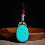 Peacock green ebony wood oval tribal necklace pendant with black veining, front view on wooden tray