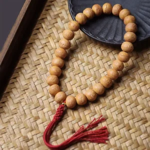 Phoenix Eye Bodhi wrist mala on bamboo mat with ceramic dish, showing natural tan beads and red tassel