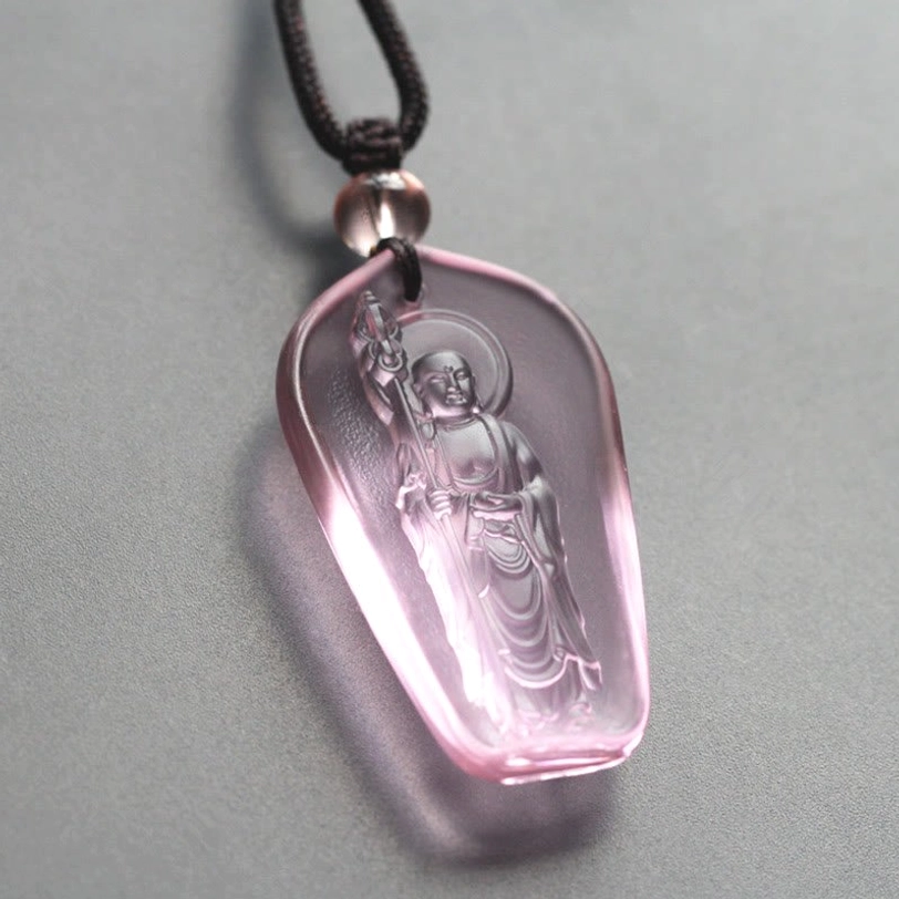 Light pink-purple Ksitigarbha Buddha Liuli crystal pendant with elongated oval shape, standing Bodhisattva with halo and staff, black braided cord with clear bead accent