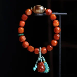 South Red Agate Pixiu Wealth Bracelet - Overhead Flat Lay with Faceted Red Agate Beads, Green Spacer Accents, and Tassel Detail on Black Background