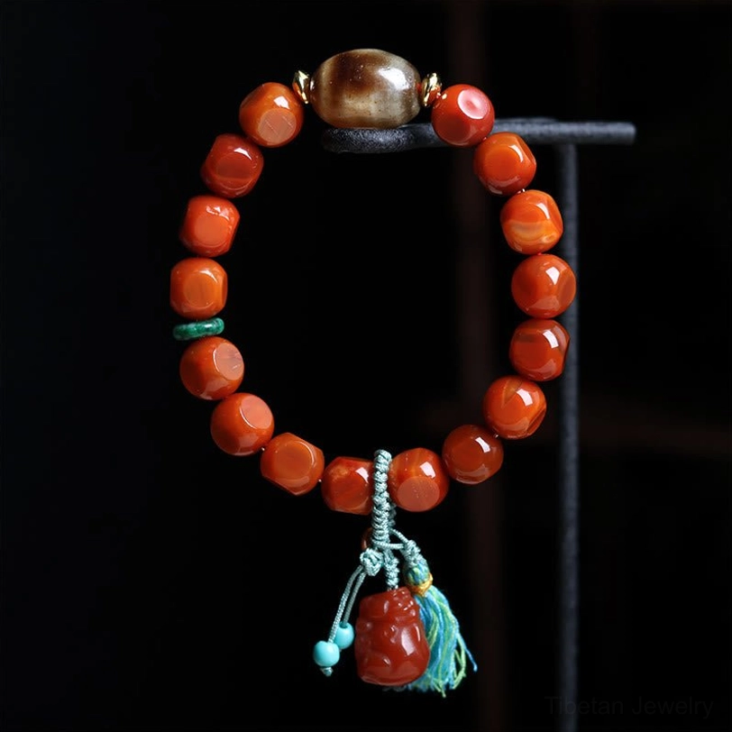 South Red Agate Pixiu Wealth Bracelet - Overhead Flat Lay with Faceted Red Agate Beads, Green Spacer Accents, and Tassel Detail on Black Background