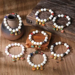 Assorted Pixiu charm bracelets with porcelain beads and gold-toned metal charms arranged on ceramic jar backdrop showing varied bead color combinations