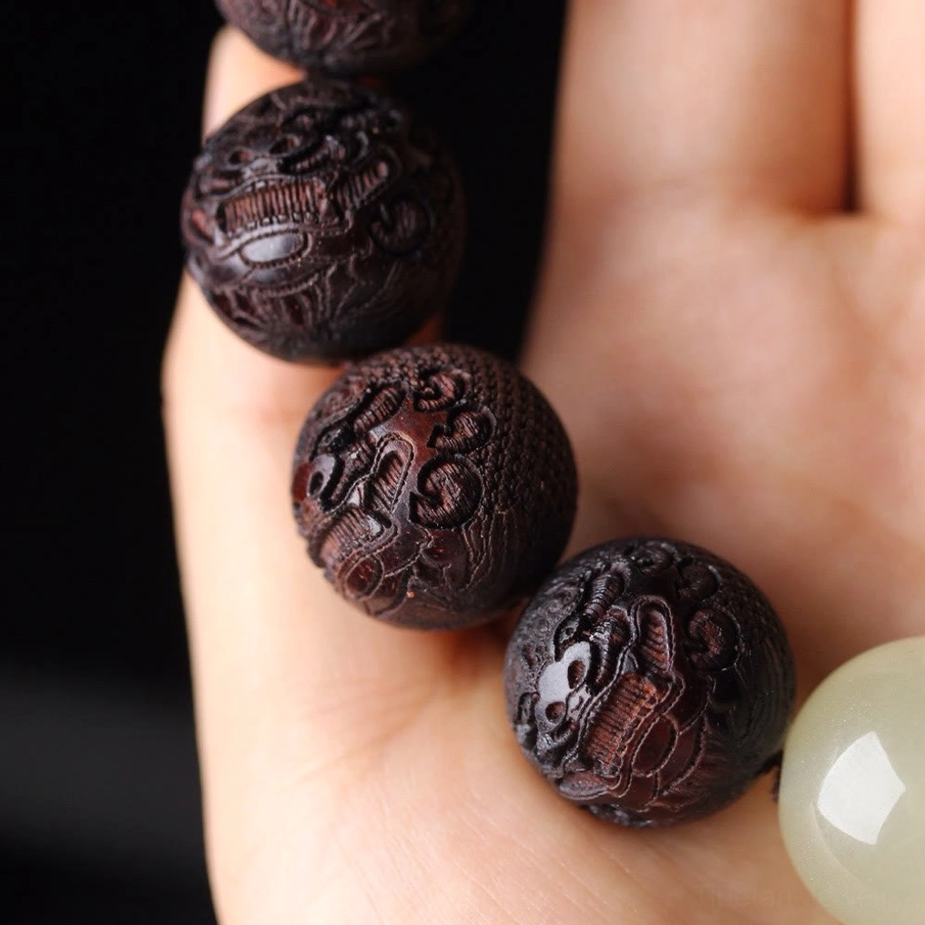 Rosewood Pixiu bracelet fingers holding beads with dark carved details on studio background