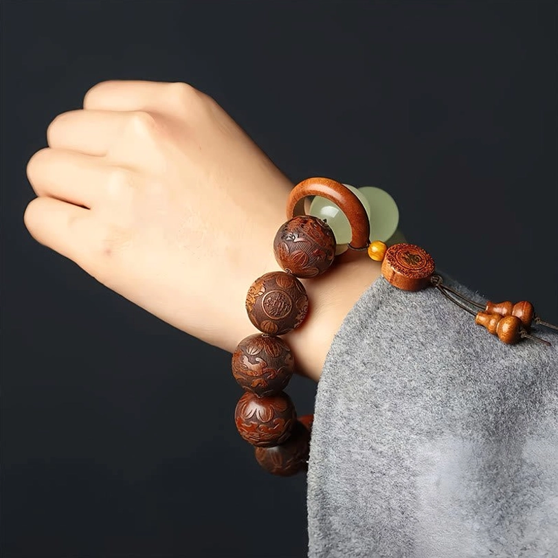 Pixiu fu wealth bracelet worn on wrist with grey sleeve on black background, showing engraved wooden beads and jade accents