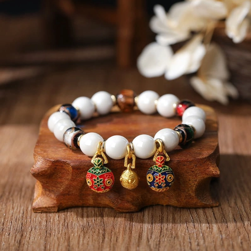 Gold Pixiu family charm bracelet with white porcelain beads and dark metal spacers featuring three distinct enamel charms on wooden stand
