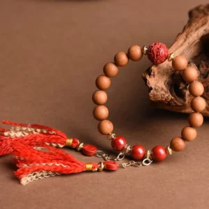 Close-up angled view of hand-carved red cinnabar pixiu bead and tan wooden beads with mixed red and beige silk tassels on craft paper