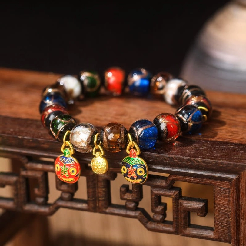 Five Elements Gold Pixiu Family Charm bracelet front close-up view featuring three gold-mounted enamel Pixiu pendants and glossy mixed-color Liuli glass beads on carved wooden edge