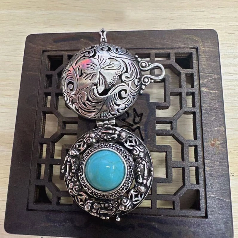 Pi Xiu locket necklace opened - top-down view showing floral engravings and reversible outer design